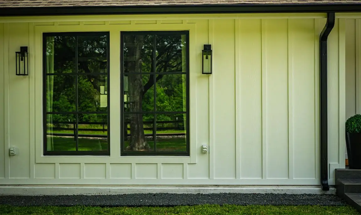 Two tall black-framed windows with grille muntins in off-white board-and-batten siding